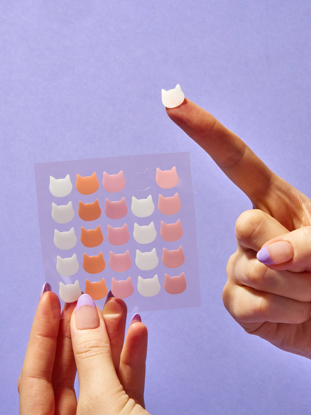 cat shaped pimple patch on model finger on purple background cat shaped pimple patch on model finger on purple background