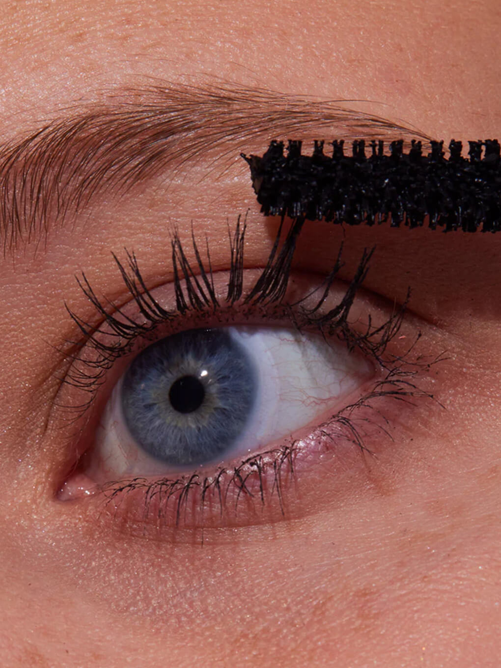 close up of model applying so extra mascara to eyelashes