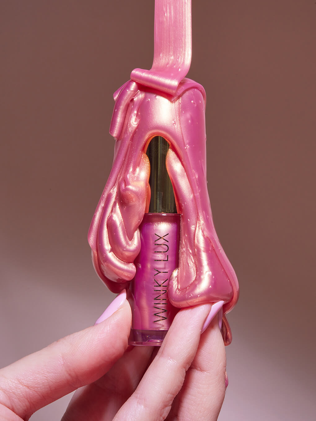 styled shot of model hand holding up pink opal lip oil with goop coming down the sides of the product