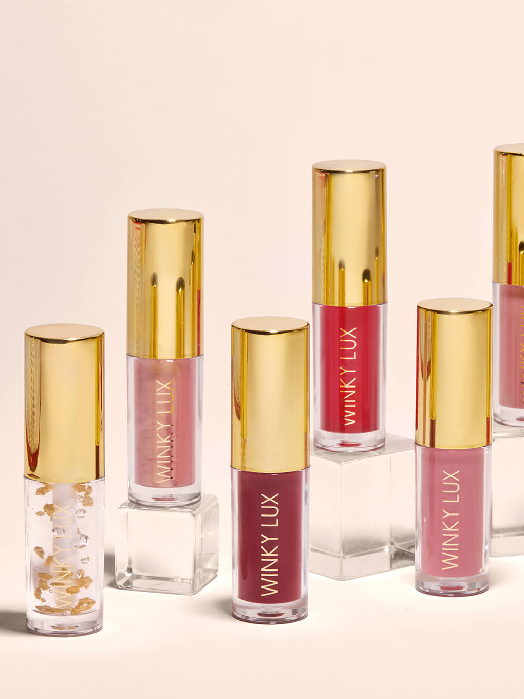 variety of lip oils in different shades with clear props against beige background