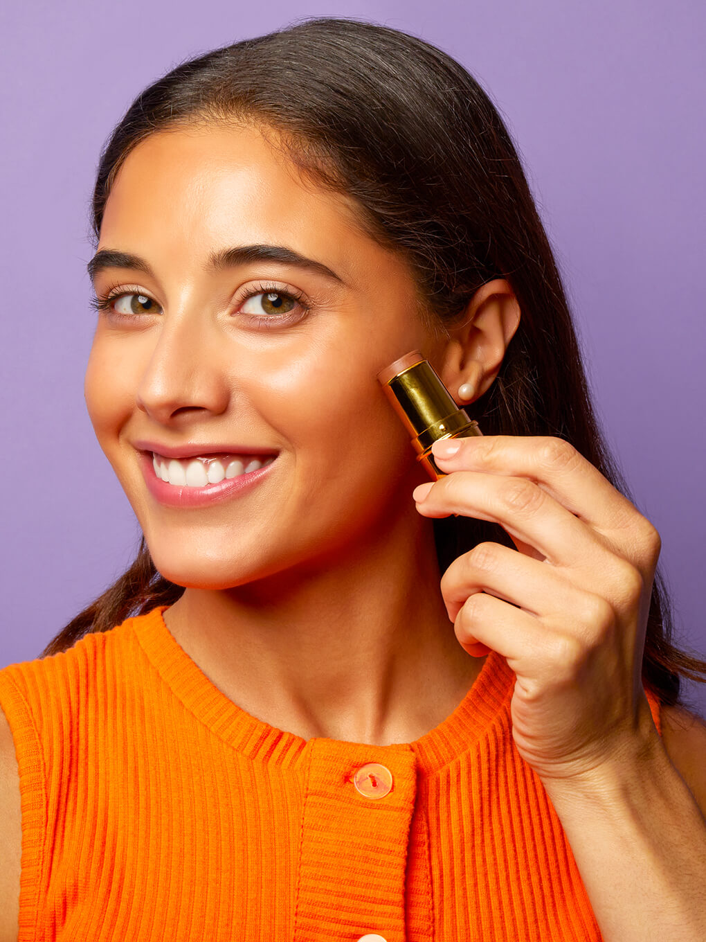 Sun Goddess -- model smiling applying bronze age cream bronzing stick to cheek bone