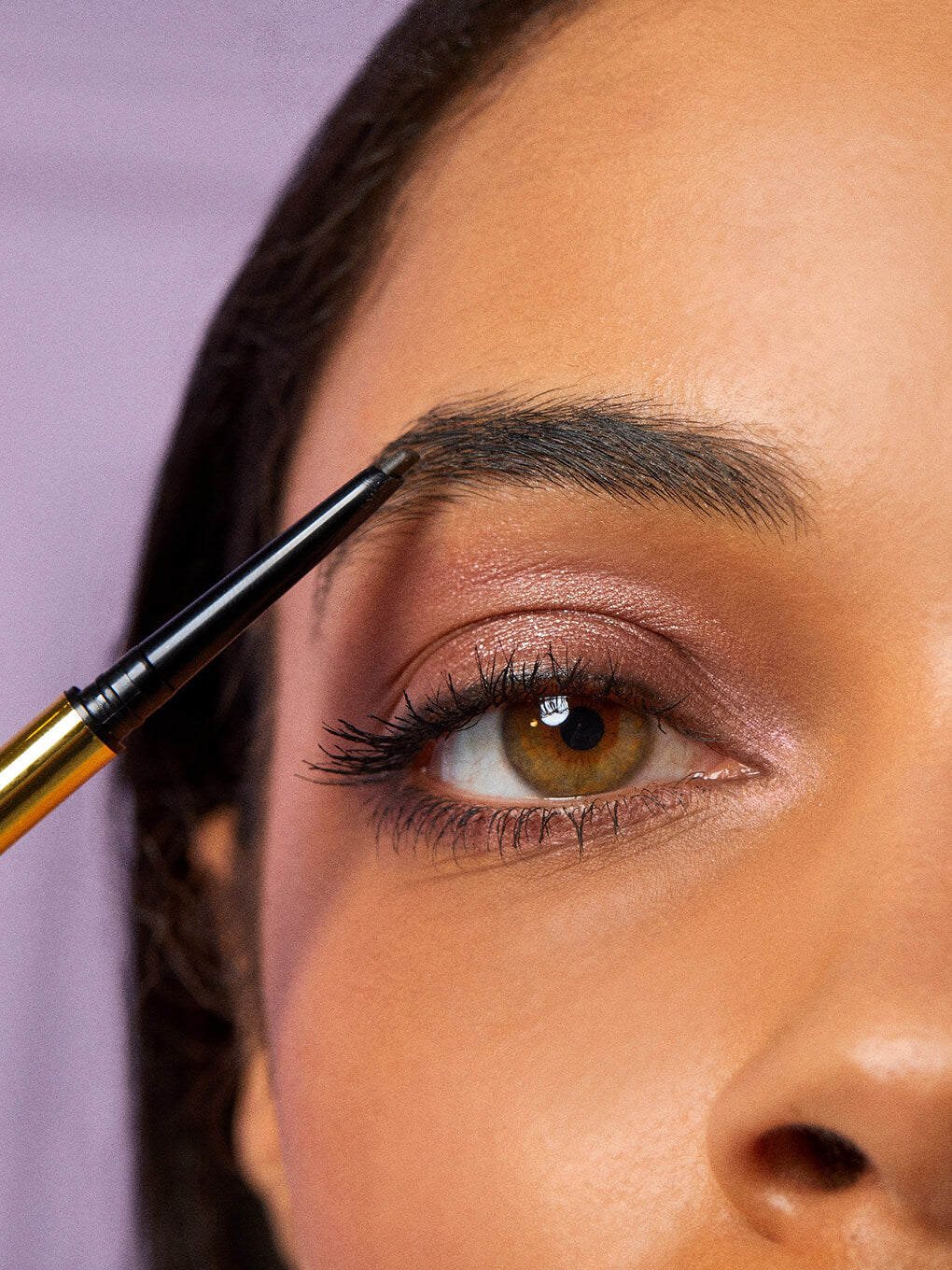 model applying unibrow precision brow pencil on purple background