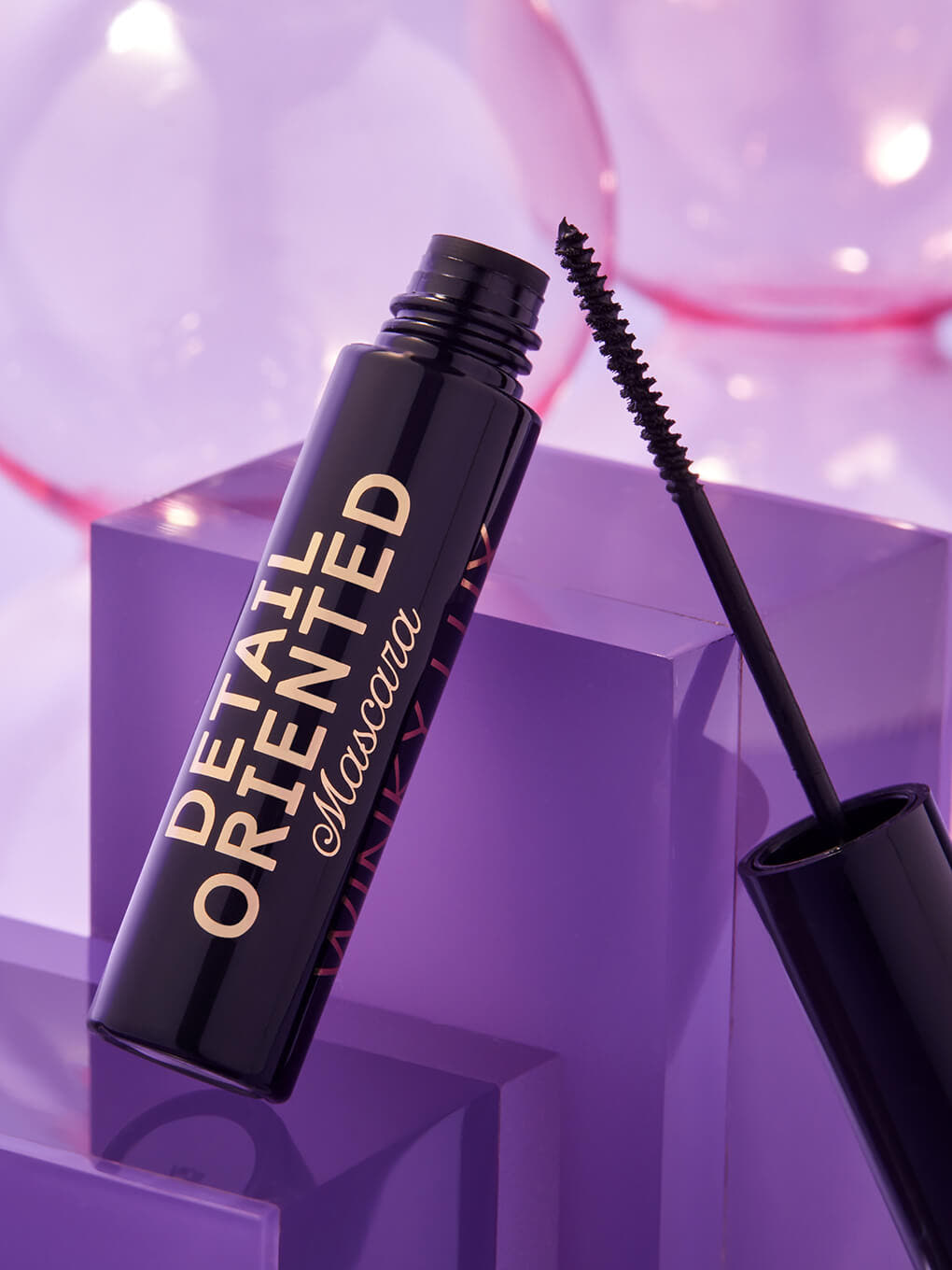 Type A Black -- detail oriented mascara component opened and leaning on glass surface on purple background