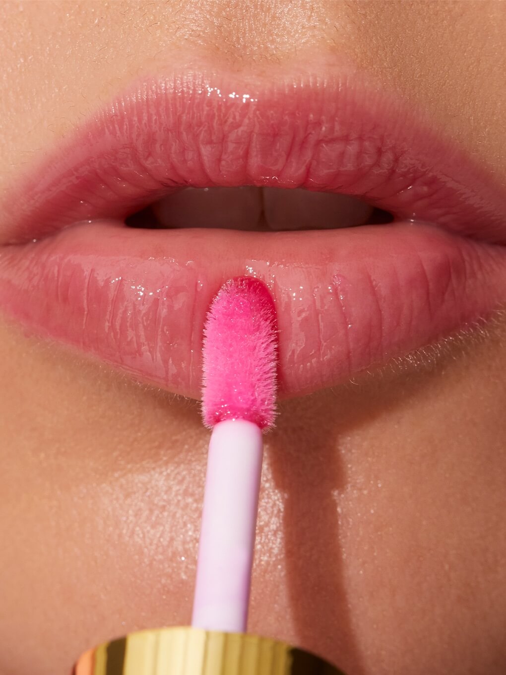 close up of pink lip oil being applied to models lips