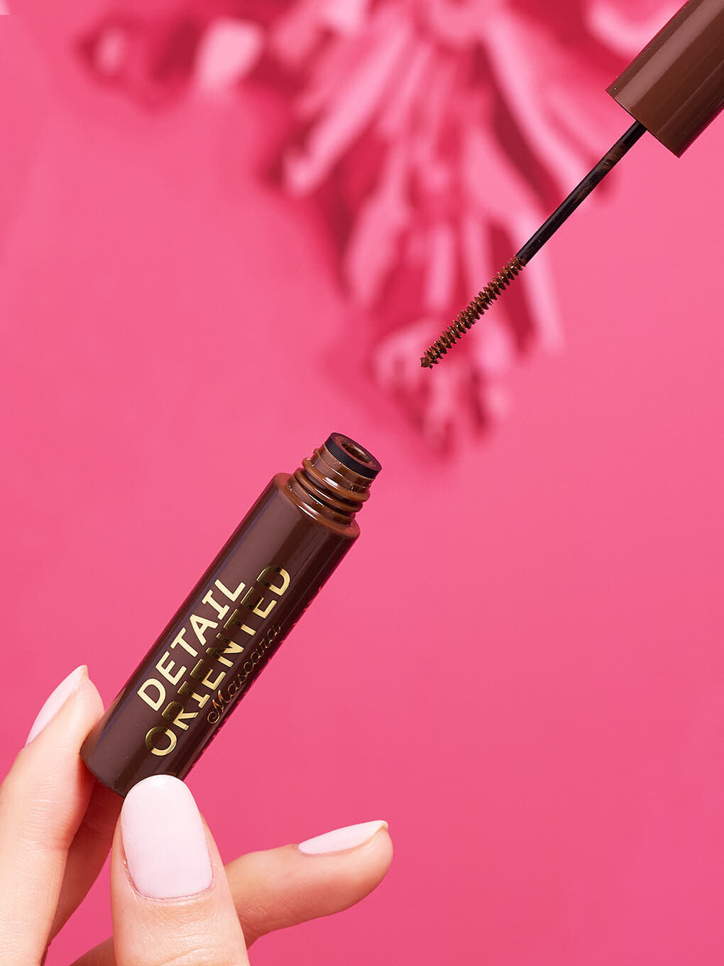 Chocolate -- close up of hand opening detail oriented brown mascara showing slender spoolie on pink background