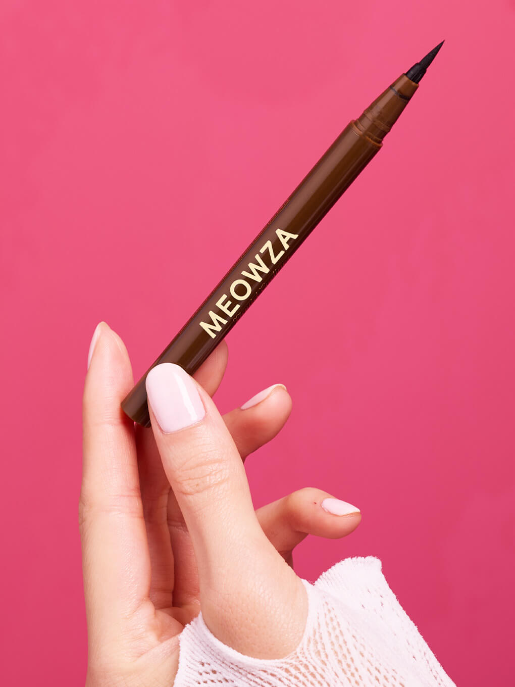 Chocolate -- hand holding brown liquid mascara on pink background