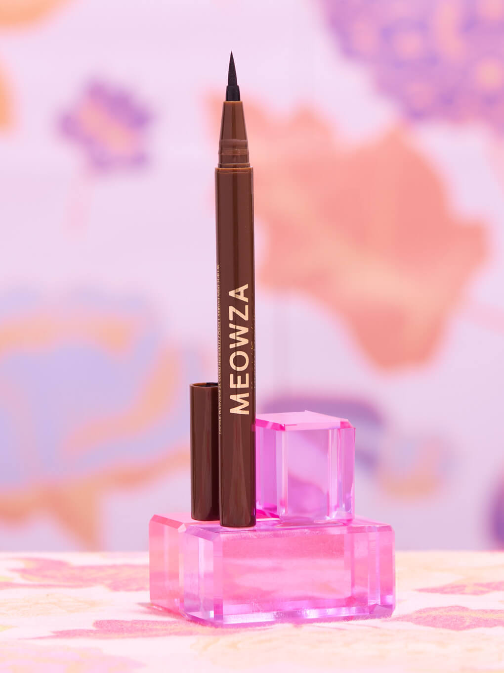 Chocolate -- stylized shot of meowza brown liquid eyeliner on pink blocks with flower wallpaper background