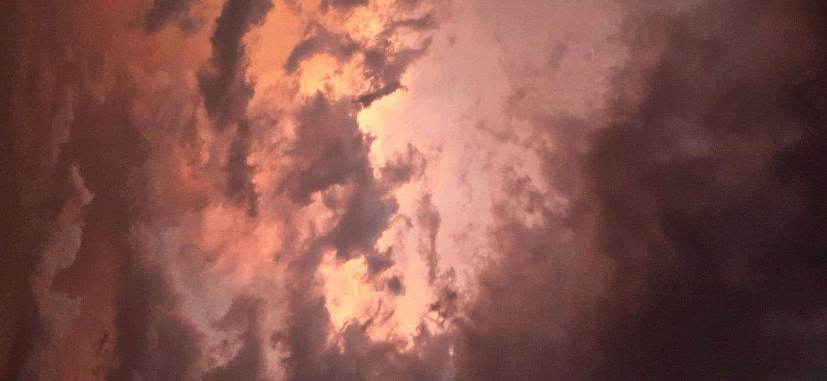 A dramatic sunset sky filled with dark storm clouds illuminated by warm orange and pink light near the horizon.