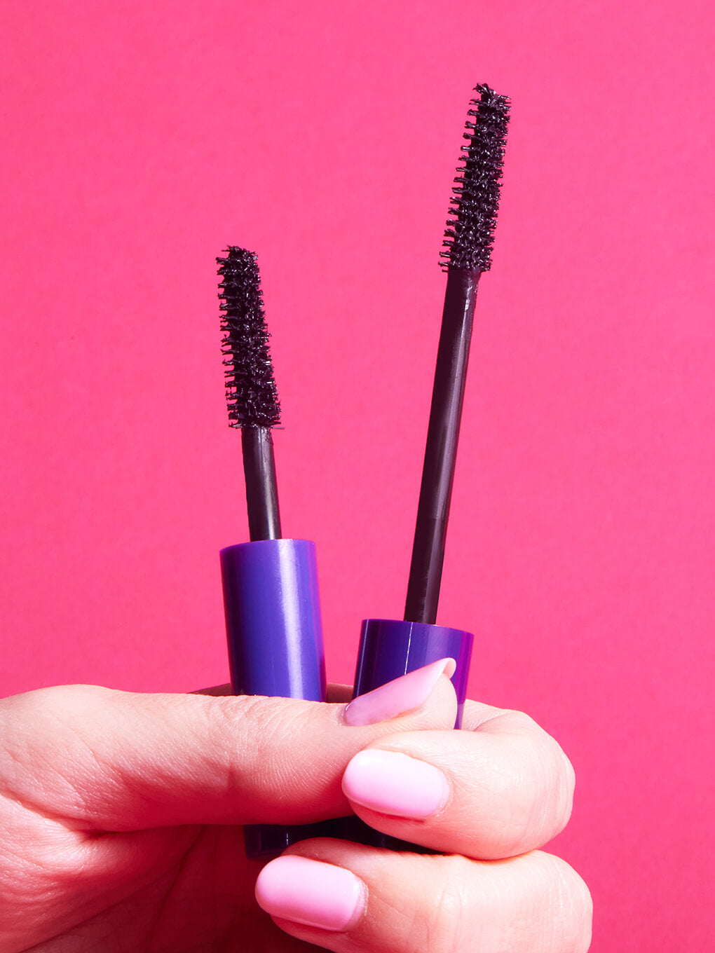 models hand holding up so extra volumizing mascara wands on pink background