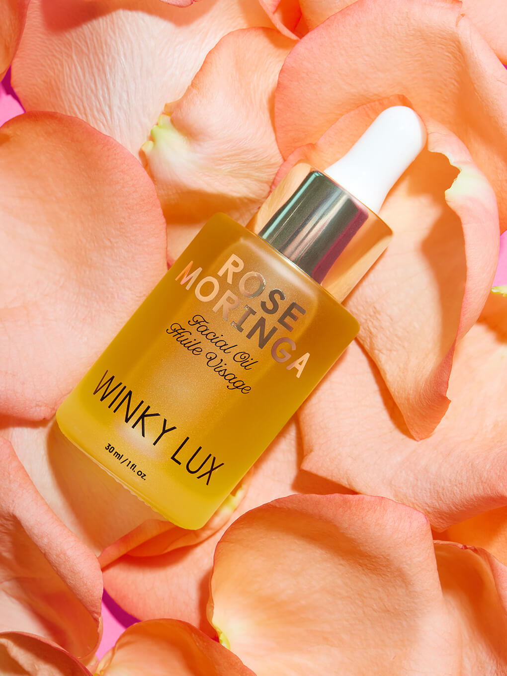 rose moringa facial oil lying in a bed of pink rose petals