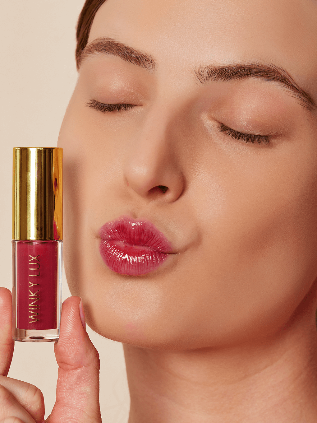 Berry -- model holding up berry pink tinted lip oil next to cheek with eyes closed