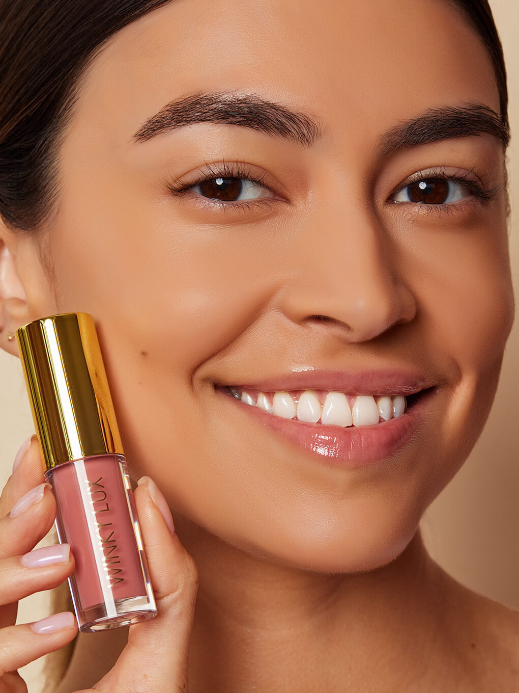 Muse -- model holding up pink tinted lip oil next to face smiling