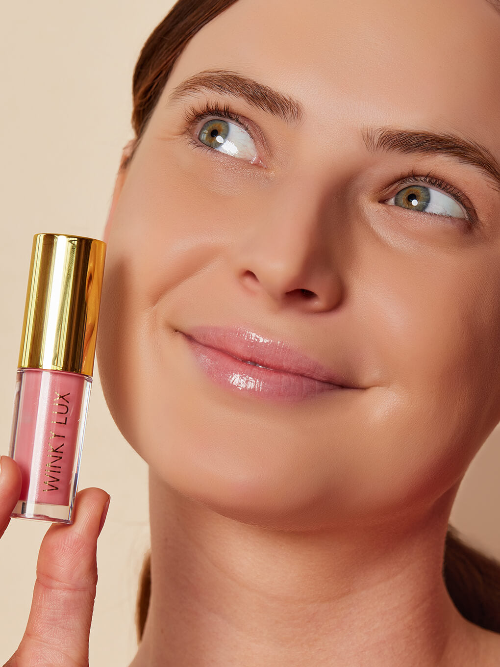 Passion -- model holding up bottle of sheer pink tinted lip oil next to cheek