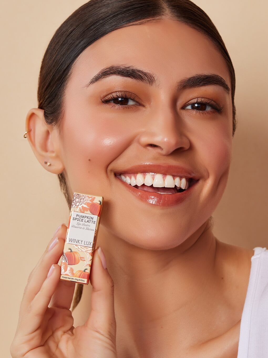 Brunette model smiling holding up pumpkin spice latte lip balm in box