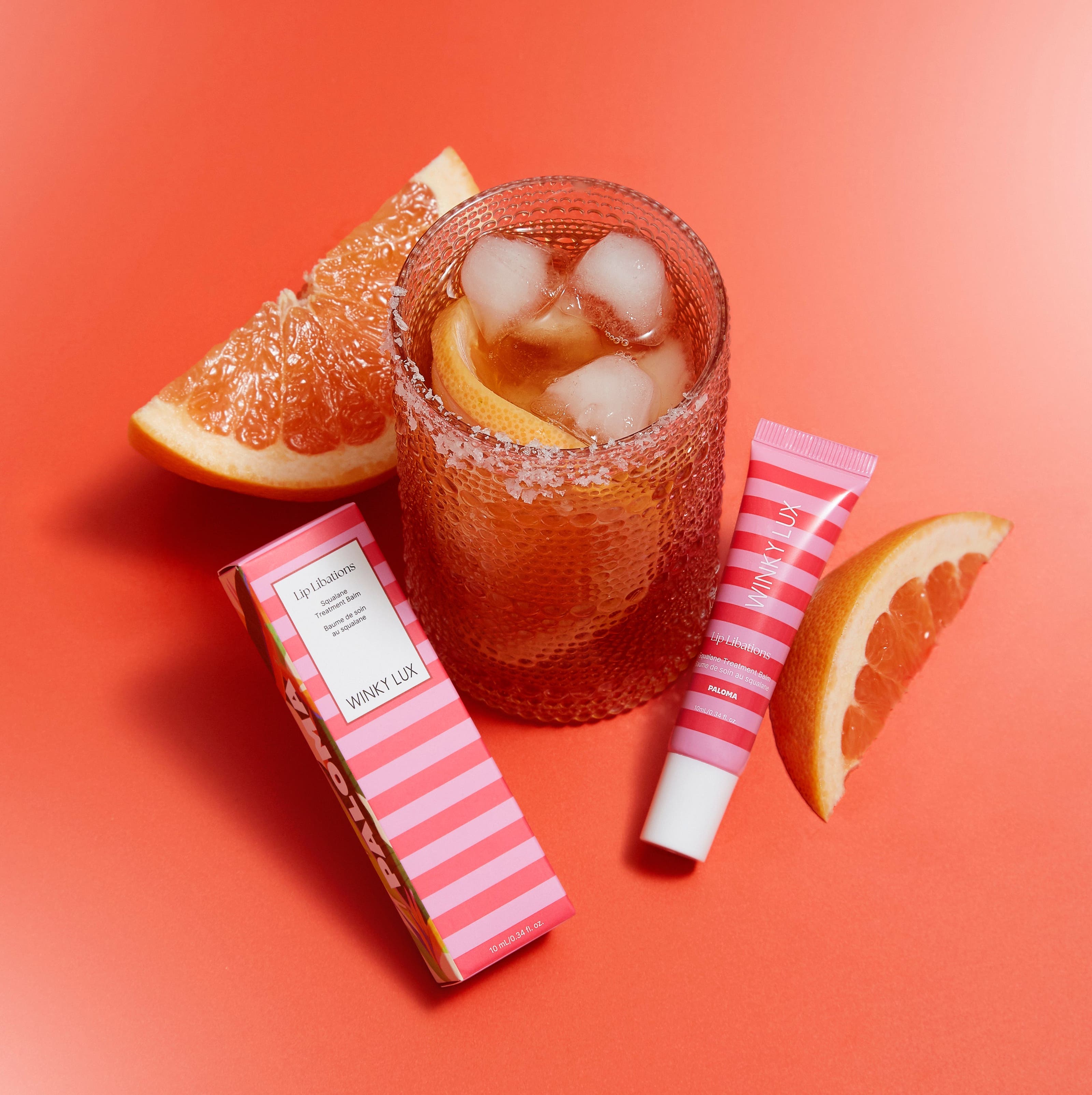 Cocktail with ice and orange slices, pink striped packets on a red background